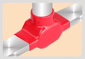 A glossy red moulded shroud closed over a tee where a round riser meets a flat conductor, bright bare metal emerging on both sides and below the moulding